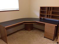 Full view of L-shaped corner desk showing black laminate top, wooden frame, and attached file cabinet with drawers on the right side.