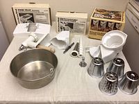 KitchenAid attachments laid out showing multiple parts including white plastic trays, metal strainer cones, and stainless steel bowl.