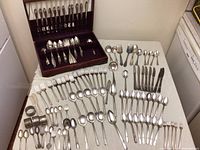 Overview of the various silverplate flatware items laid out on a table and wooden flatware box with cutlery.