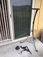 Iron metal plant stand with tripod base and curved supports next to disassembled iron deer bell parts on concrete surface