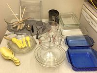 Photo showing all items included in the baking lot spread on a countertop, including glass bakeware, measuring cups, utensils, cooling racks, and flour sifter.