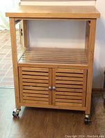 Full front view of the bamboo kitchen island showing slatted double doors, caster wheels, and lower shelf.