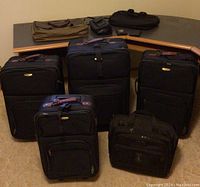 Full set of five large and medium black Skyline luggage pieces with additional smaller carry-on bags arranged on carpeted floor in front of desk.