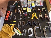 Overview of clamps, measuring tapes, and smaller hand tools including pliers, adjustable wrench, screwdrivers, knives, and gloves arranged on flat surface.