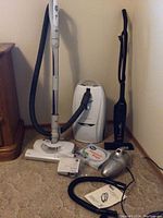 Full view of all three vacuums showing Bissell Featherweight, Progressive HEPA model, and handheld silver vacuum on carpet.