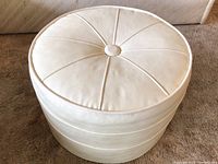 Top side view of the white round ottoman showing leather-like upholstery and stitching details with a center button.