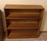 Front view of the wooden bookshelf showing three shelves and clean lines, with a medium brown wood finish.