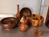 Photo showing a large segmented wooden bowl, dark wooden bowl with pedestal center, bottle-shaped vase, double-gourd wooden container with tassel, round painted fruit motif bowl, and small carved wooden shoes