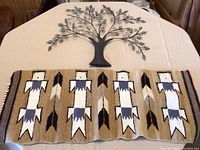Woven wall hanging and metal tree wall art displayed on table