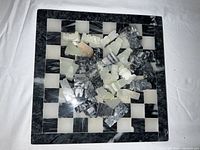 Photo shows the quartz chessboard and all the chess pieces scattered on top. The board is square with a marble-like black and white pattern. Pieces include various chess figures in black and white quartz.