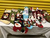 Photo showing multiple Christmas stockings with snowmen, Santa, and festive designs in various sizes and colors including red, green, beige, blue, and white.