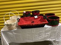 Photo of multiple Christmas themed baskets on a white cloth, showing red and green drum baskets, rectangular baskets with red lining, and natural wood baskets with white handles.