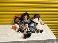 Photo showing a set of six cloth dolls arranged on a white cloth against a yellow corrugated background.