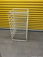 White metal wire shelving rack with 4 wire baskets and 1 slanted wire shelf shown in front of a yellow storage unit door.