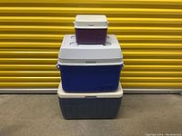 Photo showing the three coolers stacked: two large blue ones at the bottom and one small purple one on top against a yellow background