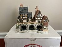 Front and side view of a large miniature cottage with three stone arches and multiple steep-roof houses above, showing detailed stone and timber work.