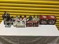 Single row of assorted ceramic and porcelain snowman figurines, some boxed musical ornaments, all arranged on a white cloth against a yellow background