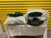 Plastic tubs and bags containing multiple faux pine wreaths and centerpieces, showing quantity and storage.
