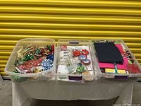 Three plastic bins filled with assorted gift wrapping items including ribbons, bows, gift bags, boxes, and tags.