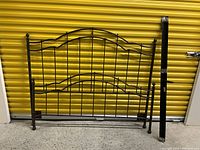 Photo showing queen-sized iron bed frame components including headboard, footboard, and rails against a yellow background.