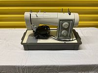 Front-side view of Kenmore Sears white sewing machine with control dials, mounted on beige base, including black foot pedal on side.