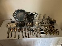 Full view of silver and brass servingware items including trays, utensils, candle holders, and decorative bowls arranged on table.