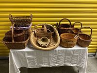 Fourteen woven baskets of different shapes and styles arranged on a table.
