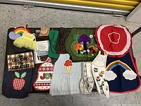 A variety of handmade fabric crafts including multiple tote bags with colorful appliques and text, aprons with various appliques and embroidery, displayed on a concrete floor.