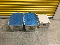 Three boxes: two large plastic bins with blue lids and one smaller cardboard box containing sewing patterns.