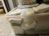 Plastic bin filled with mostly white and cream folded towels, including one visible light blue towel