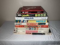 Stack of vintage board game boxes including Uno, Othello, Victory Circle, Sniggle, Sorry, Careers, Life, Monopoly, and Risk
