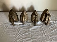 Four vintage cast iron irons painted gold, standing upright with their front pointed sides facing the camera, showing their triangular shape and twisted handles.