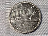 Obverse of the 1963 Canada silver dollar coin showing canoe with two paddlers, year '1963', 'CANADA' and 'DOLLAR' inscriptions.