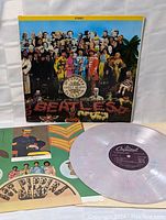 Full view of album cover with colorful artwork and Beatles floral design, record partially visible resting on the inner sleeve.