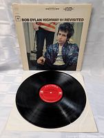 Front view of Bob Dylan Highway 61 Revisited vinyl LP record with red Columbia label visible on vinyl and album cover behind it.