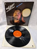 Photo of the Bob Seger Night Moves vinyl record partially pulled out of the album cover, showing the Capitol label on the record and the front of the album cover featuring Bob Seger's portrait with a round light behind him.