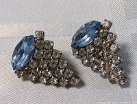 Close-up photo showing both earrings featuring blue marquise-shaped rhinestones and clear rhinestones clustered in a geometric pattern.