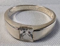 Close-up of sterling silver ring with square-cut crystal on a white textured fabric background.