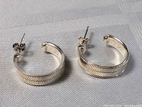 Pair of sterling silver hoop earrings with textured modernist pattern, shown from above on white fabric background.