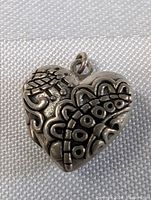 Front and side view of the heart-shaped sterling silver locket showing embossed floral and geometric patterns