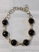 Sterling silver bracelet with six round black onyx stones on a fabric background, shown from top view with clasp and chain adjustment visible.