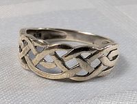Close-up of silver Celtic style ring showing the intricate knot design and polished finish on a textured surface.