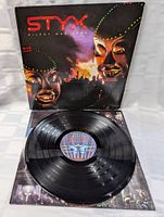 Open vinyl record on top of album cover showing the record label detail and vinyl grooves, demonstrating condition and inclusion of the record.