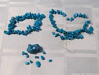 Two strands of turquoise chip beads and some loose turquoise chunks laid out on a light cloth background.