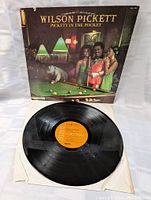 Vinyl record with an orange side A label visible, placed in white protective sleeve.