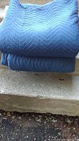 Two blue quilted moving blankets folded and placed on stone steps.