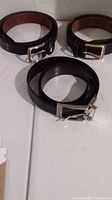 Photo of all three black leather belts rolled up, showing different buckles and tan inner lining