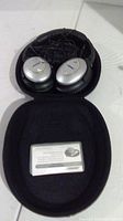 Bose QuietComfort 15 headphones folded inside black hard carrying case with instruction card visible