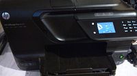 Front angle of HP Officejet Pro 8600 printer showing output tray extended and power button lit.