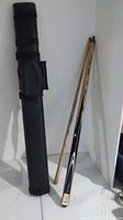 Photo of the two-part wooden pool cue and black carrying case standing upright against a wall